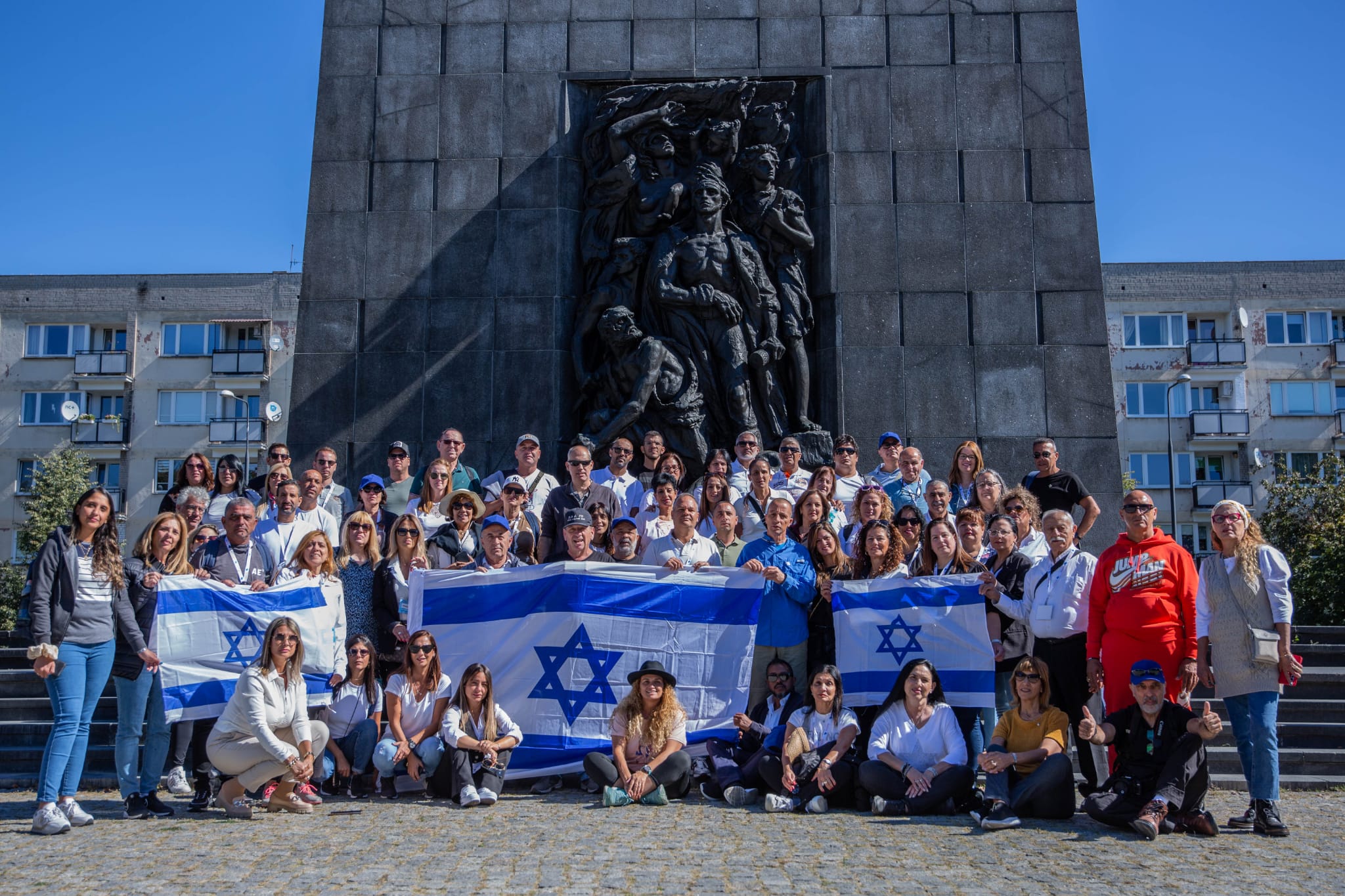 משלחת גדולה עם דגלי ישראל מצטלמת מול אנדרטת מרד גטו ורשה