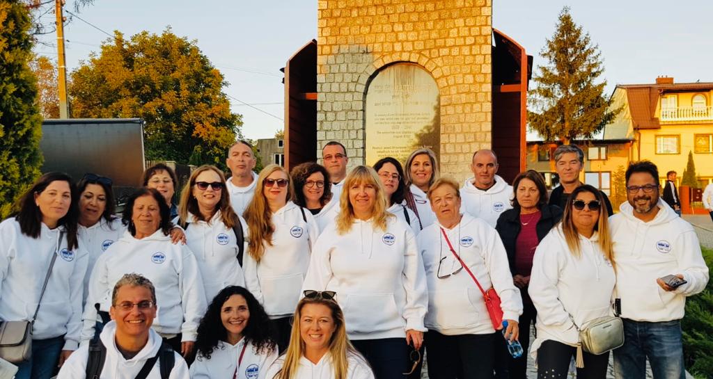 קבוצת משלחת ארגונית בחולצות זהות מצטלמת לצד אנדרטה בעיירה פולנית