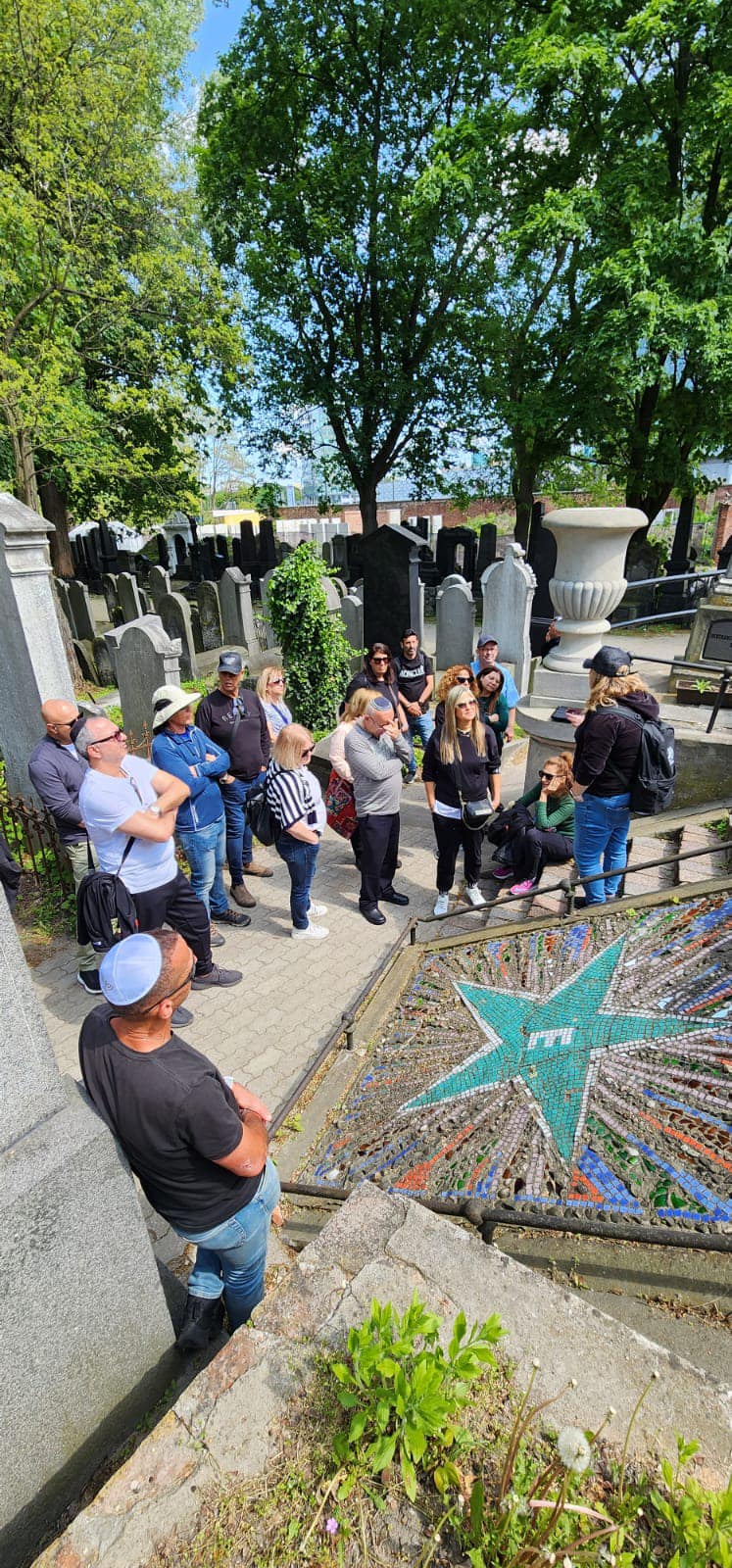 קבוצת מבוגרים מתבוננת במצבת פסיפס בבית עלמין יהודי בפולין