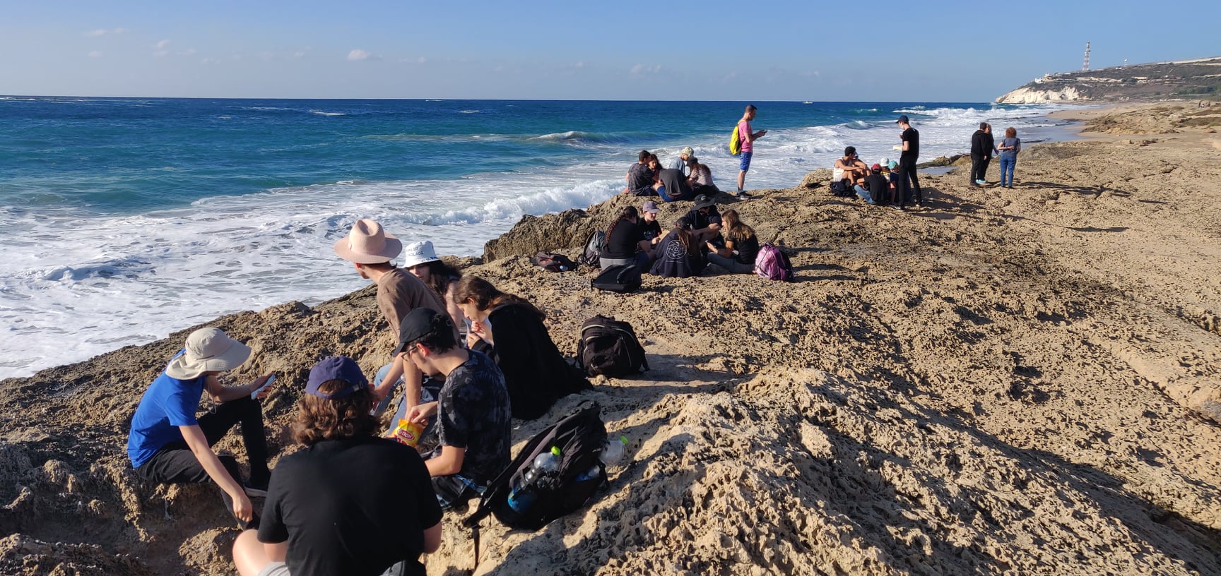 תלמידים לומדים בקבוצות קטנות על סלעי חוף מול הים התיכון