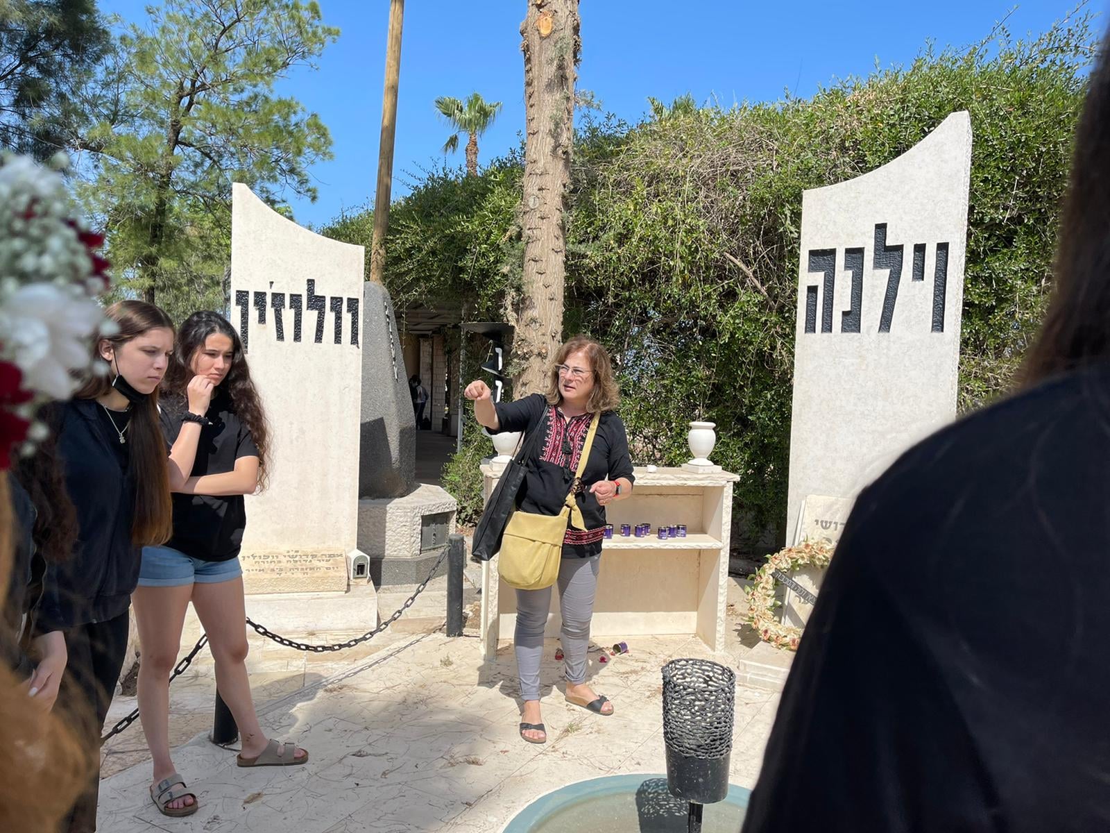 מדריכה בבית עלמין מצביעה על אנדרטאות לזכר קהילות וילנה ווולוז׳ין