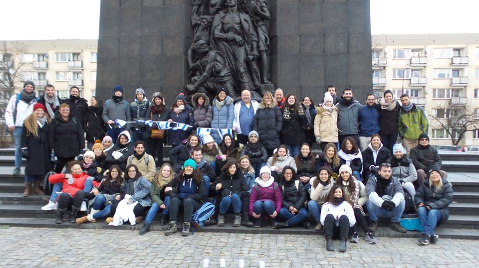 משלחת סטודנטים רחבה מצטלמת מול אנדרטת מרד גטו ורשה בחורף