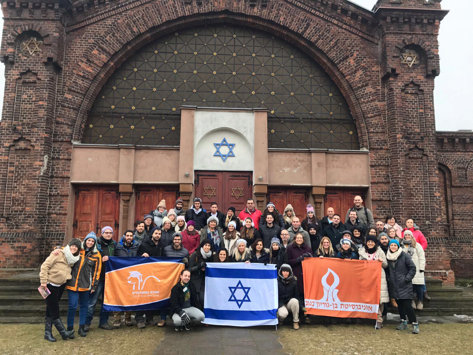משלחת סטודנטים ממוסד אקדמי עם דגלי ישראל לצד בית כנסת היסטורי