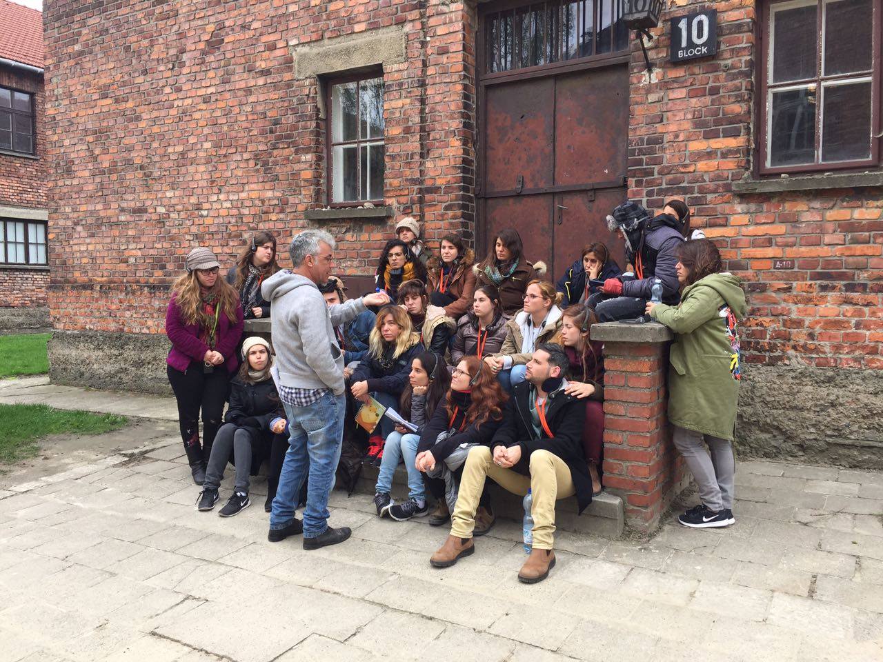 מדריך מול נבו מסביר לקבוצת סטודנטים ליד בלוק 10 באושוויץ