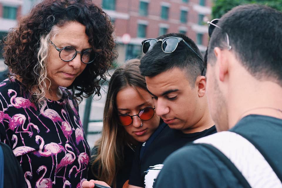 מדריכה ותלמידים מתכנסים סביב מסך טלפון בסמטה עירונית