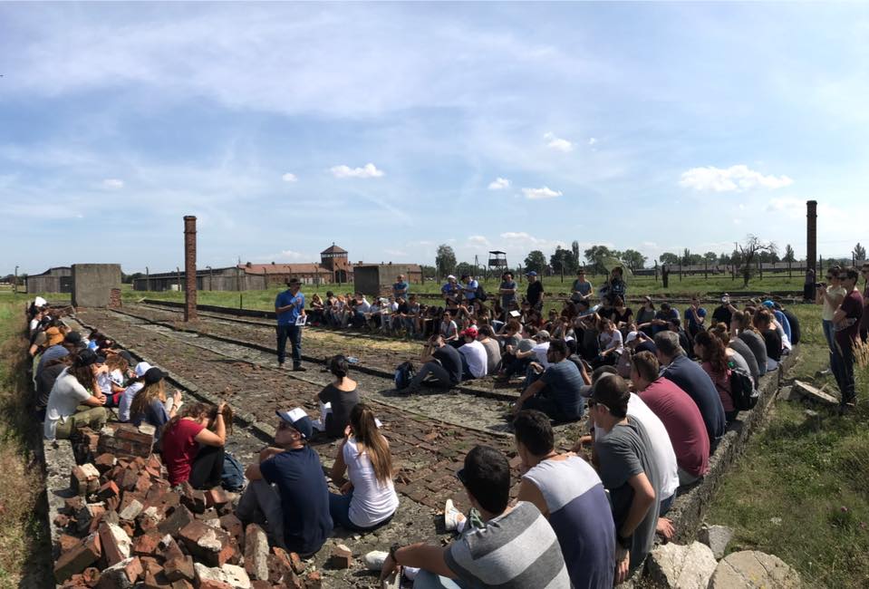 קבוצת בני נוער יושבת במעגל דיון ליד מסילות הרכבת בבירקנאו